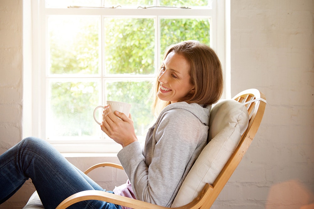 Une femme souriante assise buvant une tasse de thé